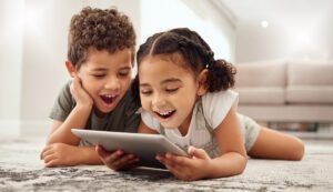 Two kids watching a video excitedly on a tablet while laying on the floor.